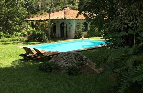 Correas Casa | Casa colonial con otras dos casas más pequeñas en el borde de un río y por el bosque.